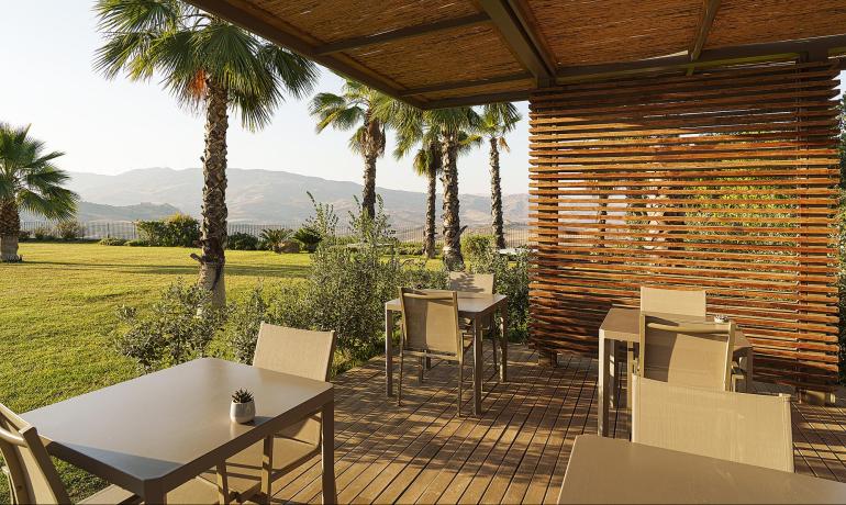 Terrazza con tavoli, palme e vista montagna al tramonto.