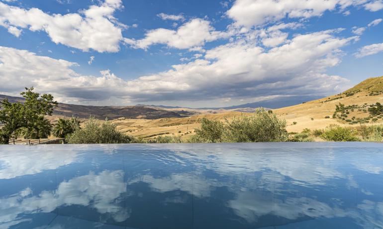 Piscina riflette cielo azzurro e colline dorate, creando serenità infinita.