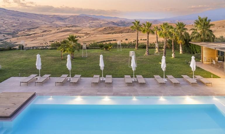 Piscina serena con vista su colline dorate e palme al tramonto.
