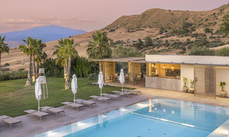 Piscina elegante con vista collinare al tramonto, palme e atmosfera rilassante.