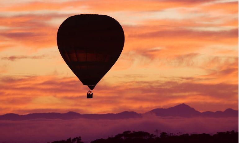 Mongolfiera al tramonto, cielo infuocato e montagne serene.