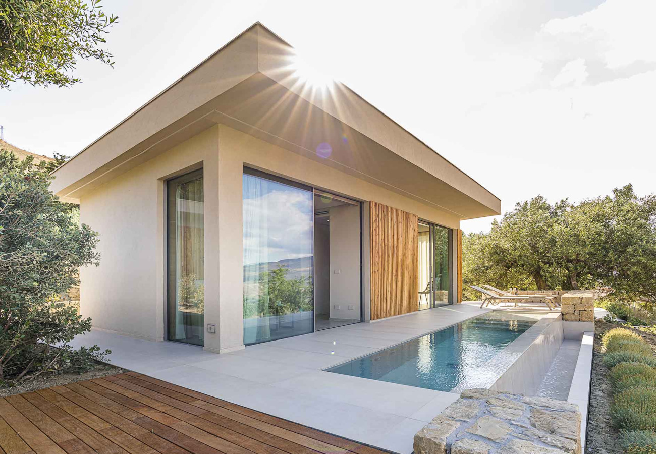 Moderna villa con piscina, ampie vetrate e terrazza in legno, immersa nella natura.