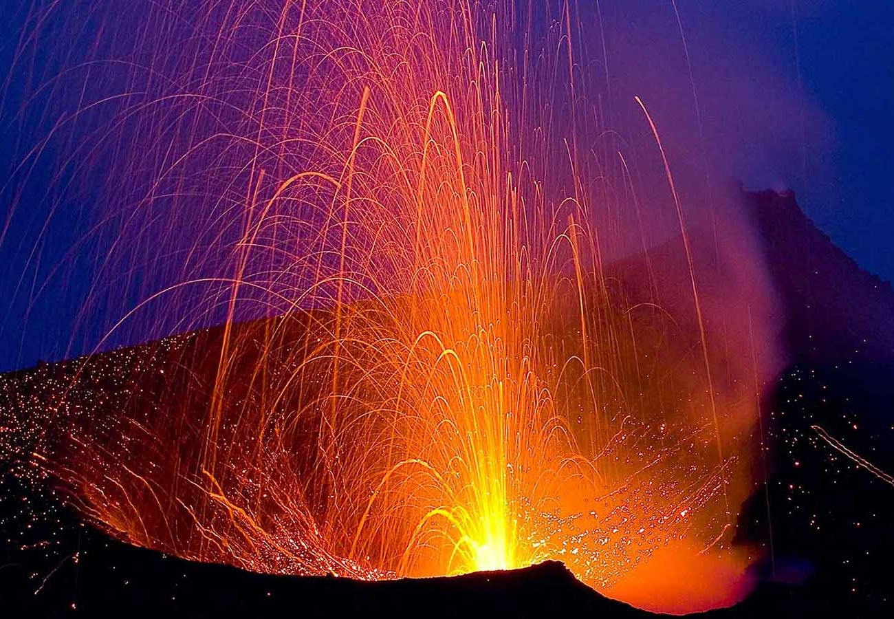 Eruzione vulcanica con lava incandescente e scintille sotto un cielo notturno.