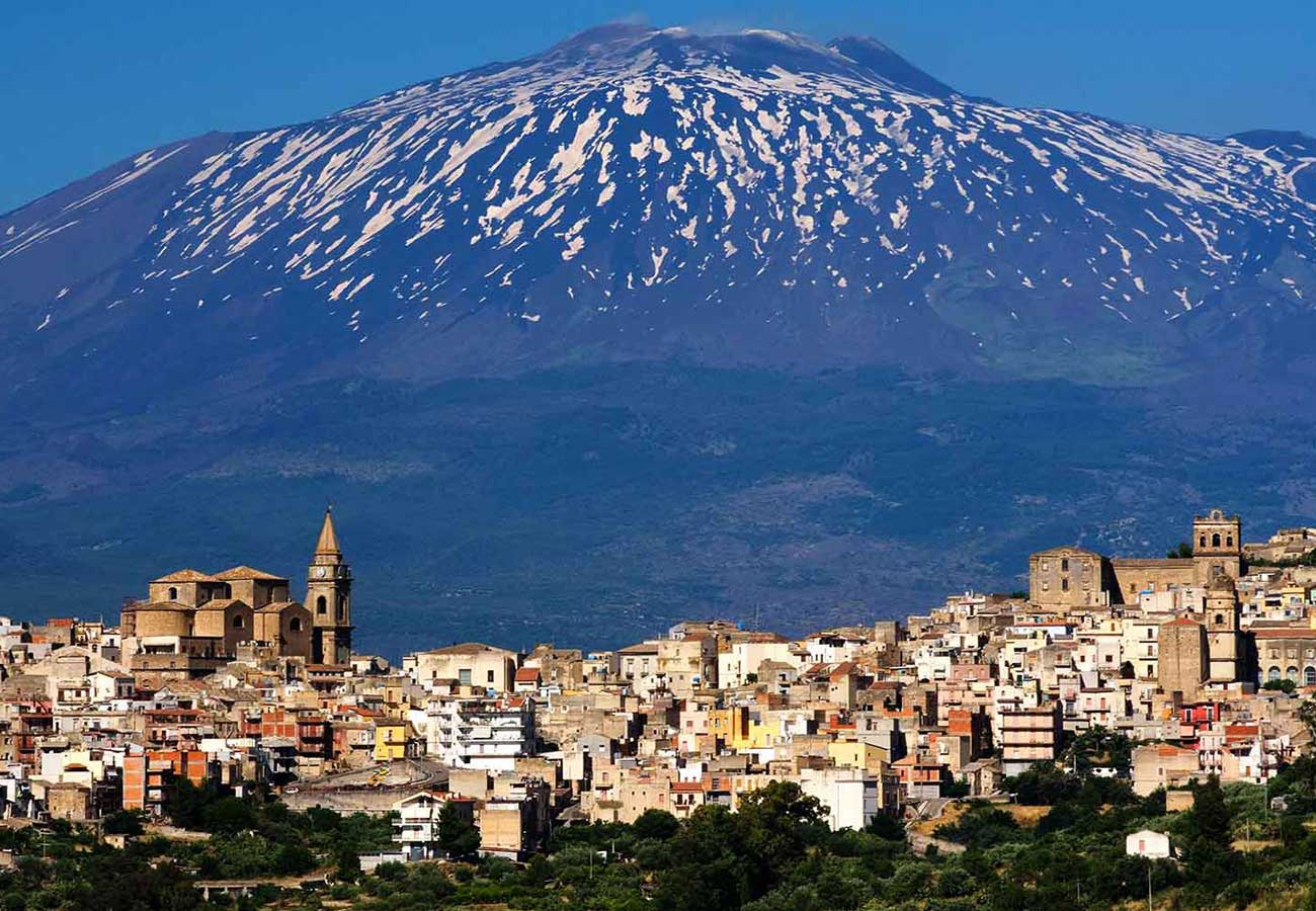 Paesaggio con città storica e maestoso vulcano innevato sullo sfondo.