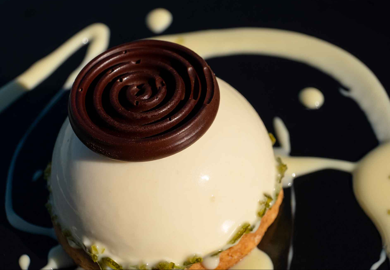 Dessert a cupola con decorazione al cioccolato e crema su piatto nero.