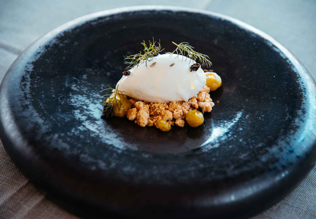 Dessert gourmet con gelato, crumble e frutti decorativi su piatto nero elegante.