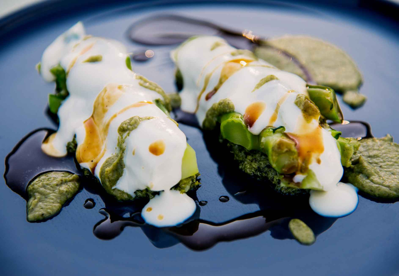 Piatto gourmet con crema verde, salsa bianca e guarnizione su piatto blu.