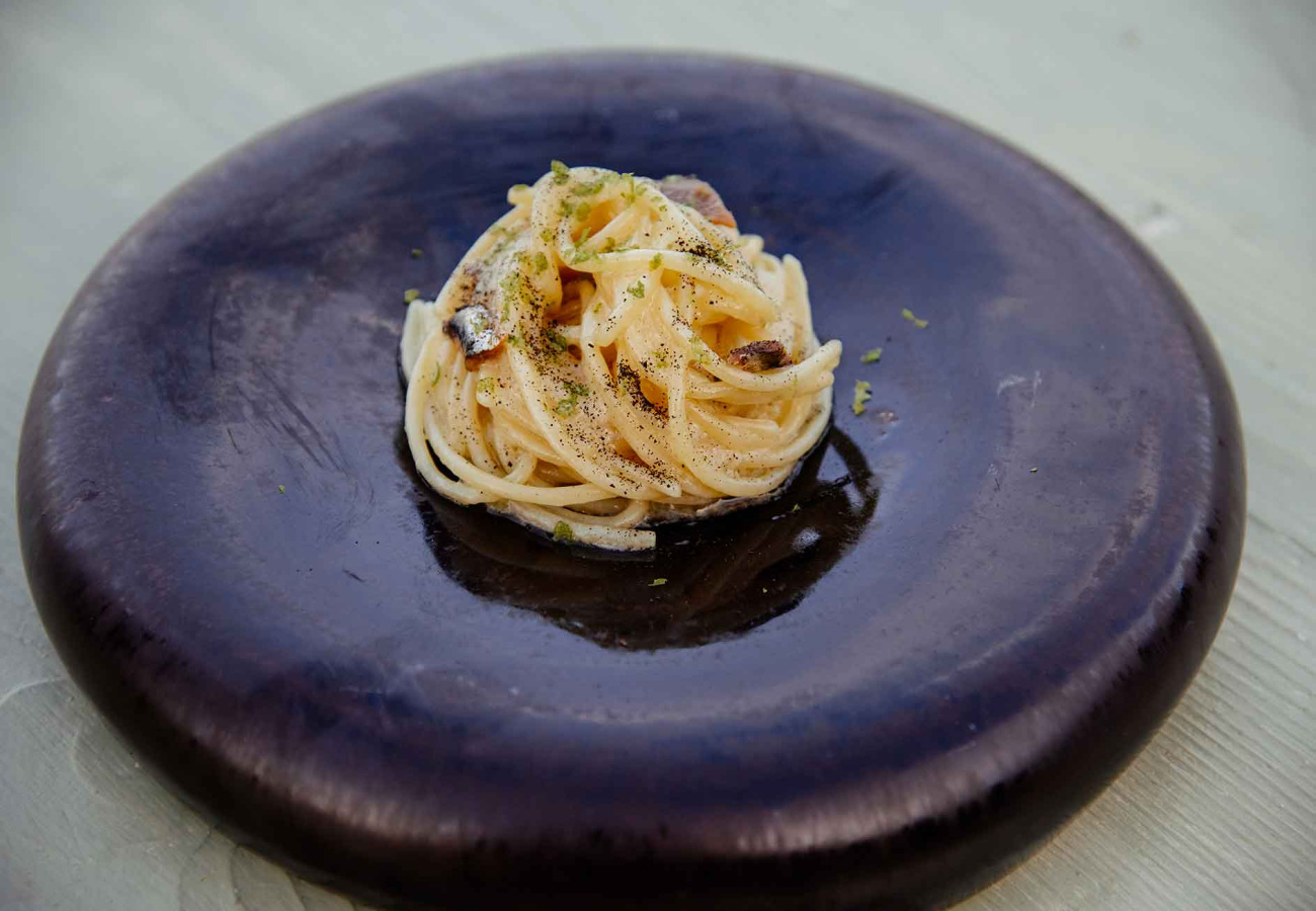 Spaghetti cremosi con pepe nero e guarnizione su piatto scuro elegante.