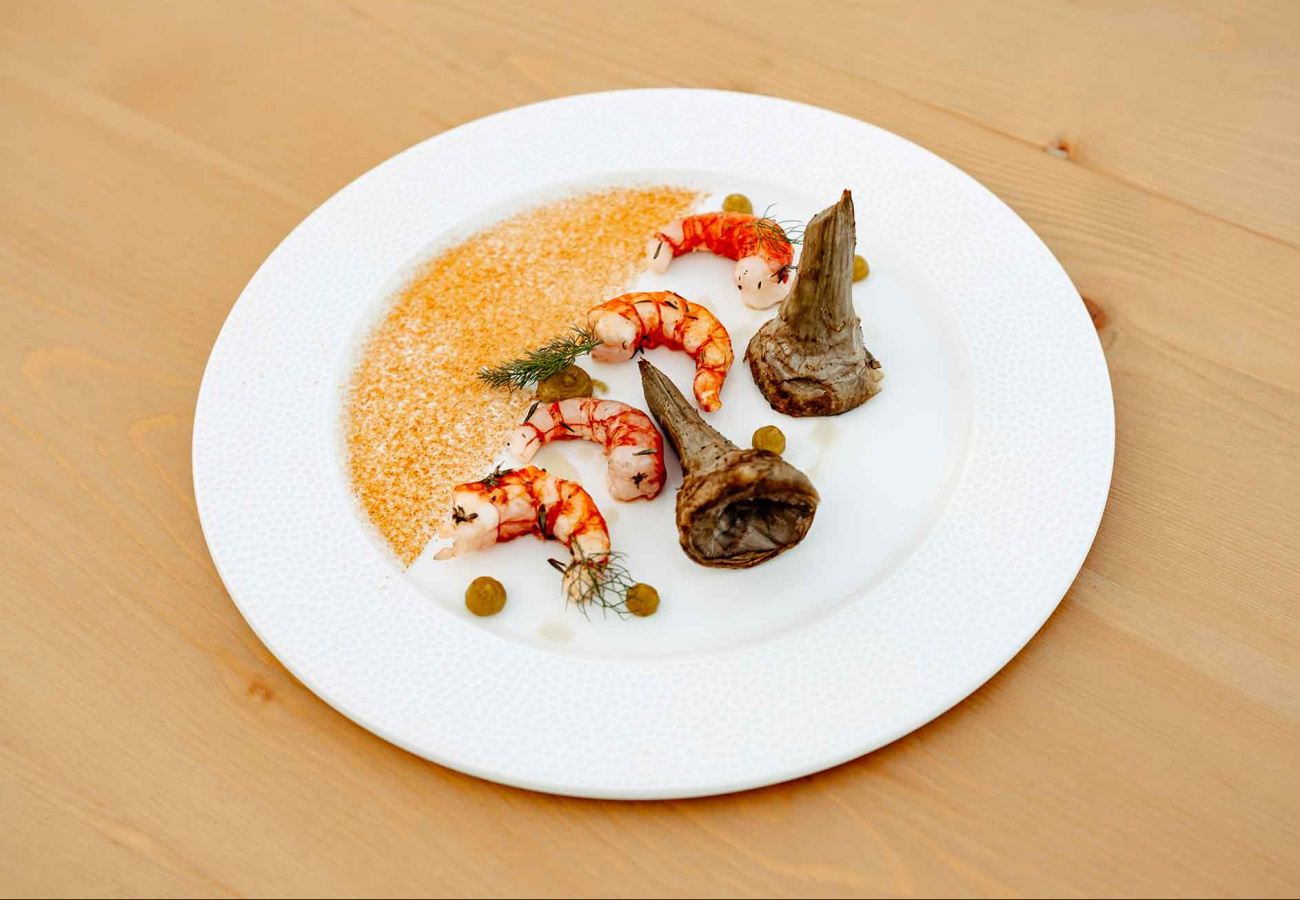 Piatto raffinato con gamberi, carciofi e salsa su piatto bianco elegante.