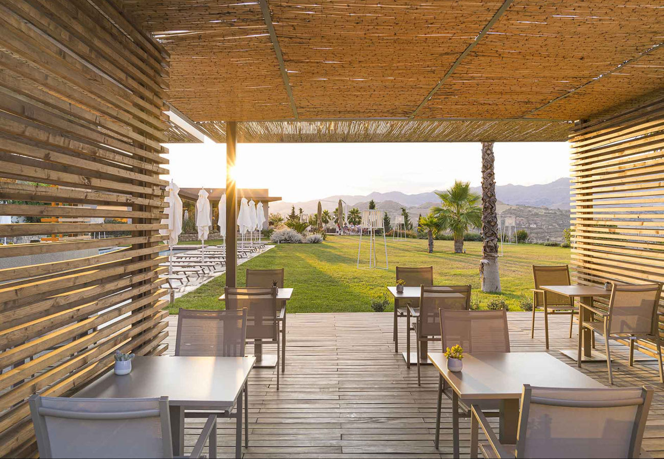 Terrazza con tavoli, vista su prato e montagne al tramonto.