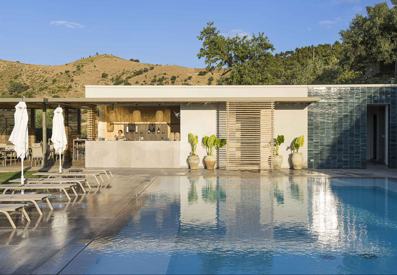 Piscina moderna con bar all'aperto, sedie a sdraio e paesaggio collinare.