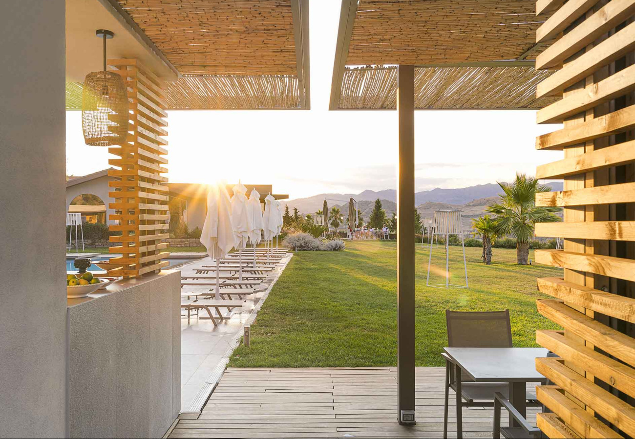 Terrazza con vista su piscina, prato e montagne al tramonto.