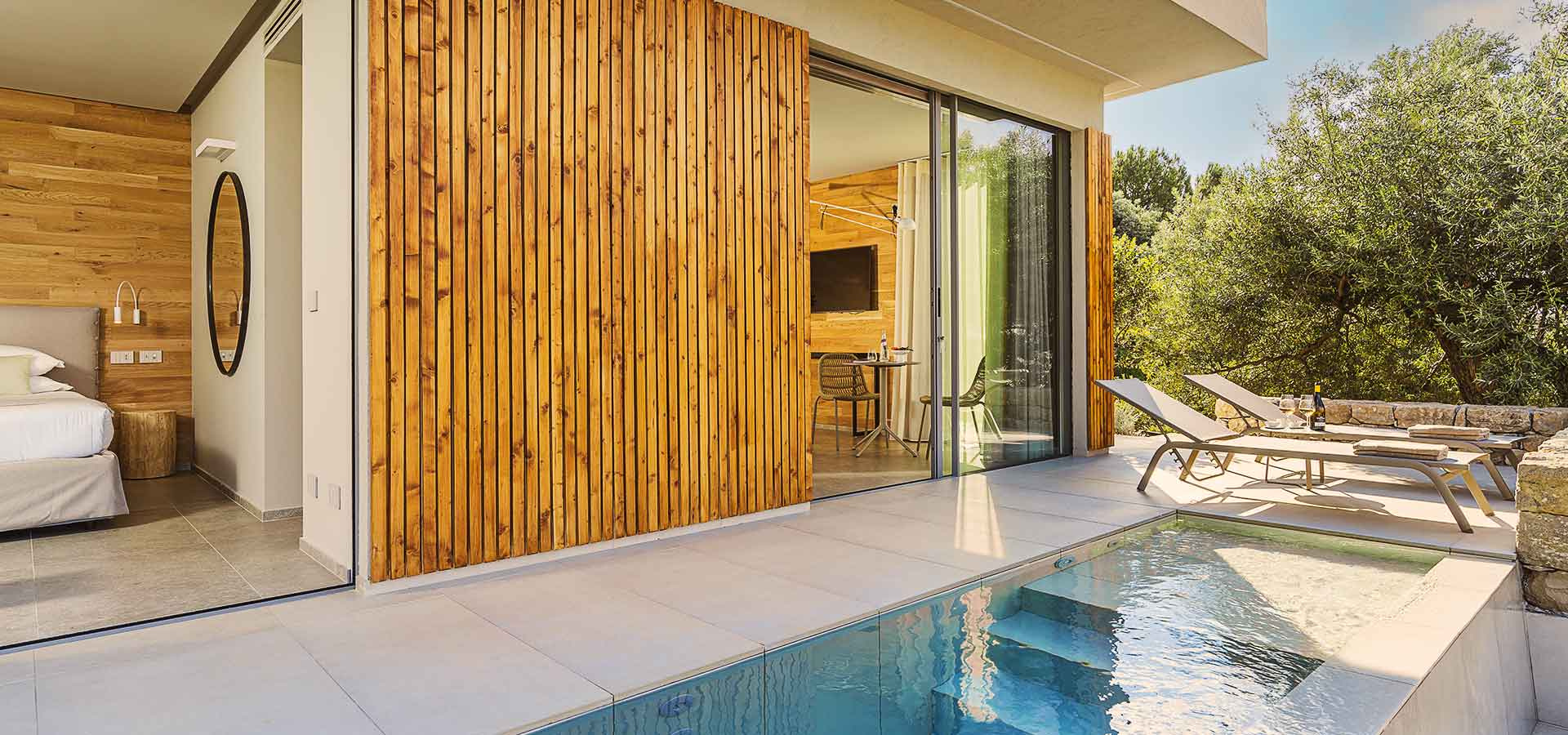Moderna camera con piscina privata, arredi in legno e terrazza con lettini.