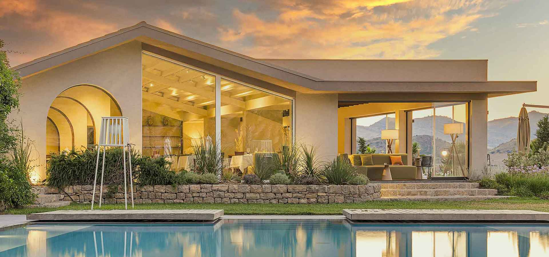 Villa moderna con ampie vetrate, piscina e vista panoramica al tramonto.