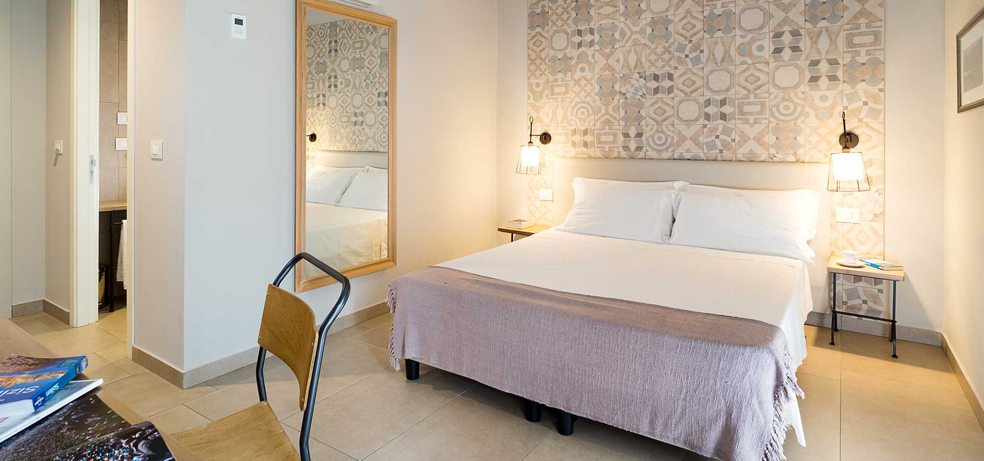 Camera moderna con letto matrimoniale, specchio e decorazioni geometriche alle pareti.