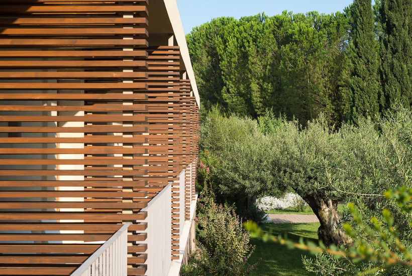 Facciata in legno con giardino verde e alberi sullo sfondo.
