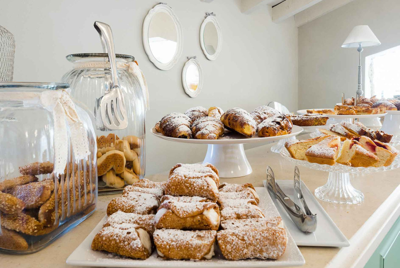 Buffet con dolci assortiti, tra cui cannoli, croissant e biscotti in barattoli di vetro.
