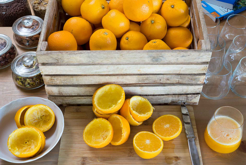 Cassetta di arance, spremute fresche, bicchieri e frutta secca su tavolo.
