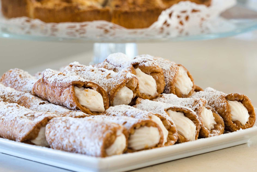 Cannoli siciliani con crema dolce e zucchero a velo su un piatto bianco.
