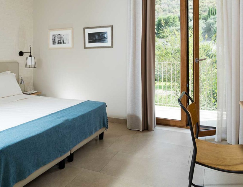 Camera moderna con letto, sedia, e porta finestra che apre su un giardino.
